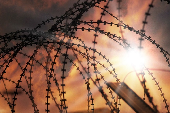 Barbed wire over prison wall at sunset